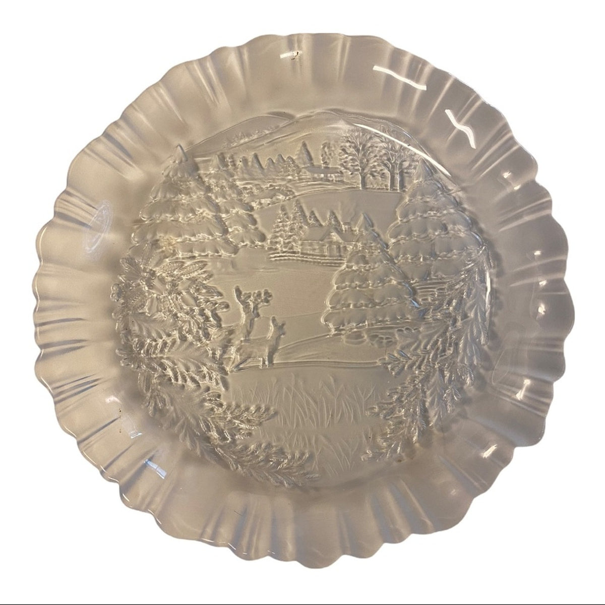 A scalloped-edge clear glass plate featuring an embossed winter landscape design in the center, shown against a plain white background.