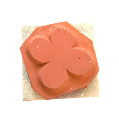 A rubber stamp of a 4 leaf clover or a flower, shown on a light beige textured backing against a white background.