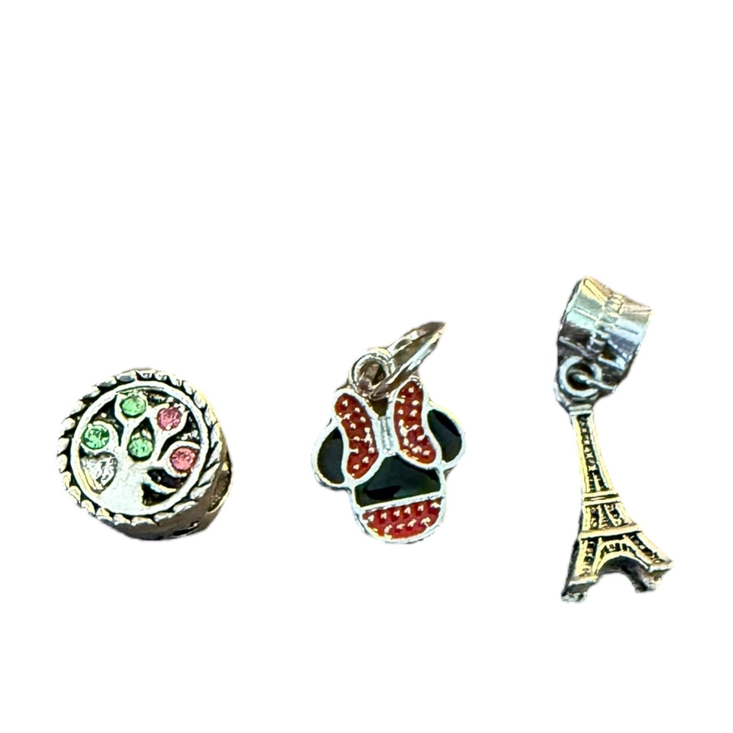 Three charms: a round charm with green and red details, a skull-shaped charm with red and black details, and an Eiffel Tower charm on a white background.