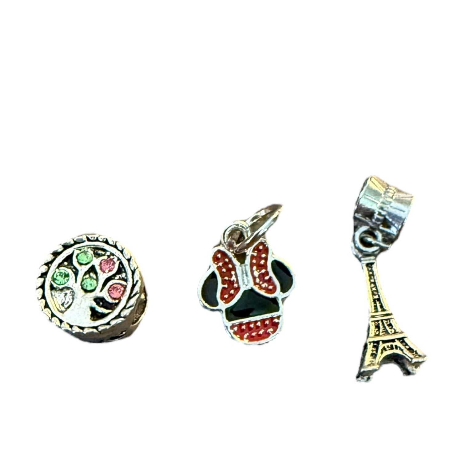 Three charms: a round charm with green and red details, a skull-shaped charm with red and black details, and an Eiffel Tower charm on a white background.