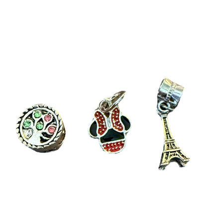 Three charms: a round charm with green and red details, a skull-shaped charm with red and black details, and an Eiffel Tower charm on a white background.