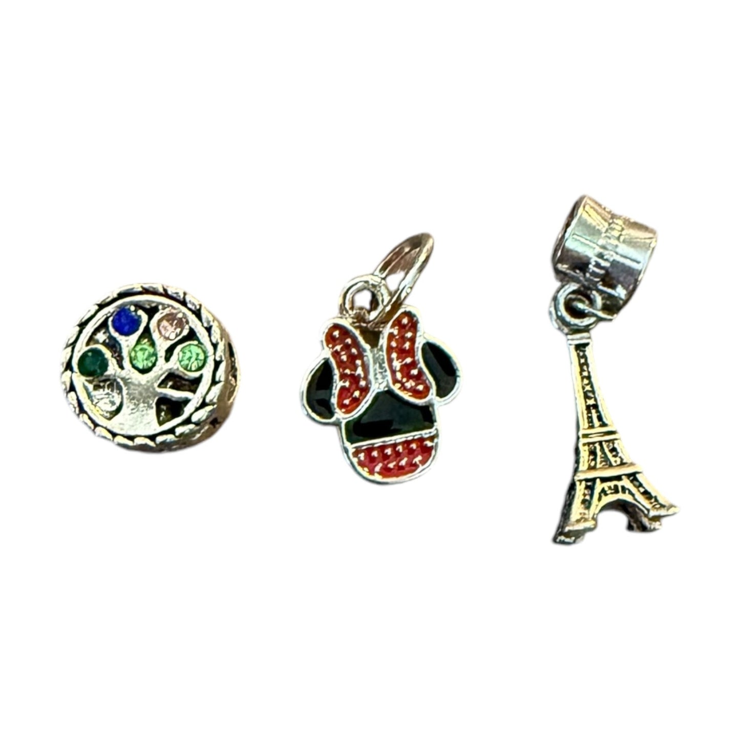 Three charms: a round multicolored gemstone charm, a red and black bow charm, and a gold Eiffel Tower charm, on a white background.