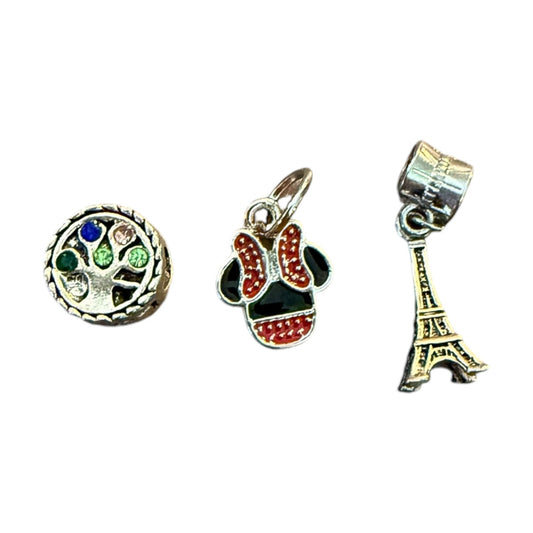 Three charms: a round multicolored gemstone charm, a red and black bow charm, and a gold Eiffel Tower charm, on a white background.