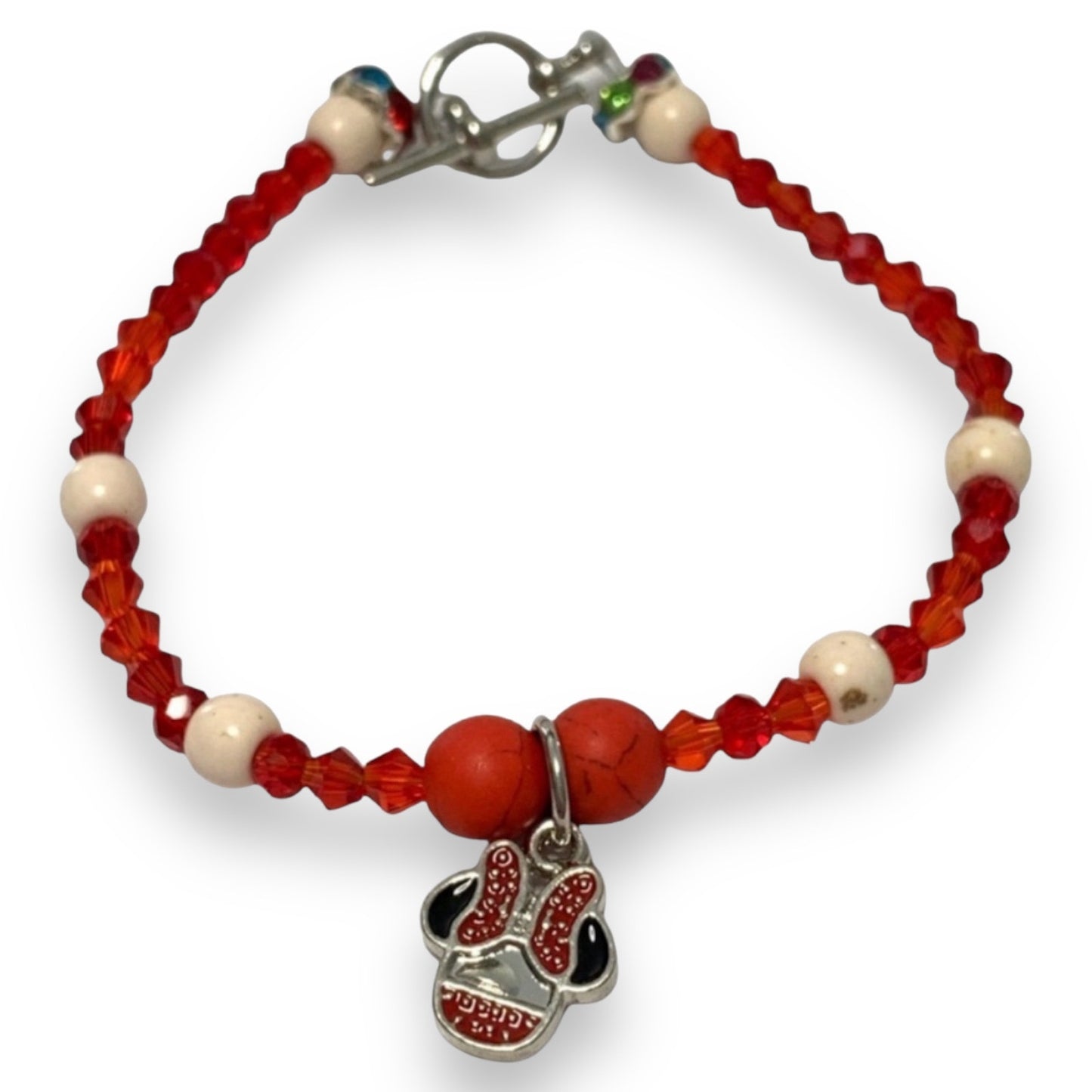 A beaded bracelet featuring red faceted beads, white round beads, a red and black bow charm, and a silver-toned lobster clasp, shown on a plain white background.