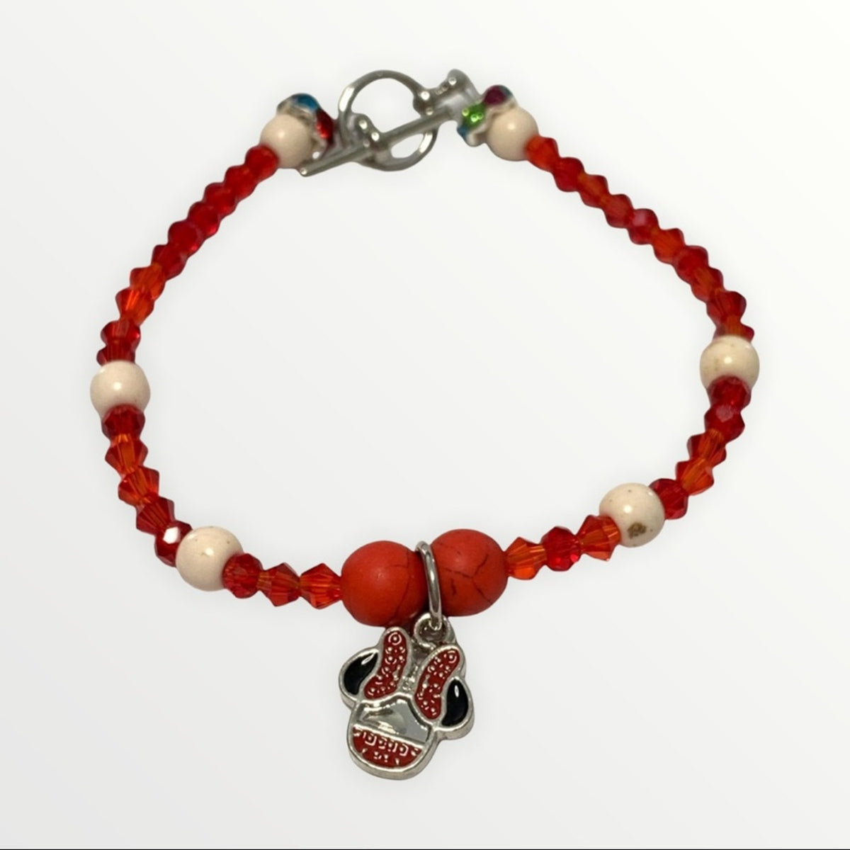 A beaded bracelet featuring red faceted beads, white round beads, a silver clasp, and a dangling charm shaped like a baseball with red and black glitter-like detailing.