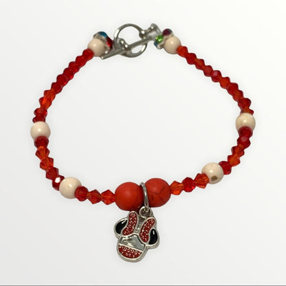 A beaded bracelet featuring red faceted beads, white round beads, a silver clasp, and a dangling charm shaped like a baseball with red and black glitter-like detailing.