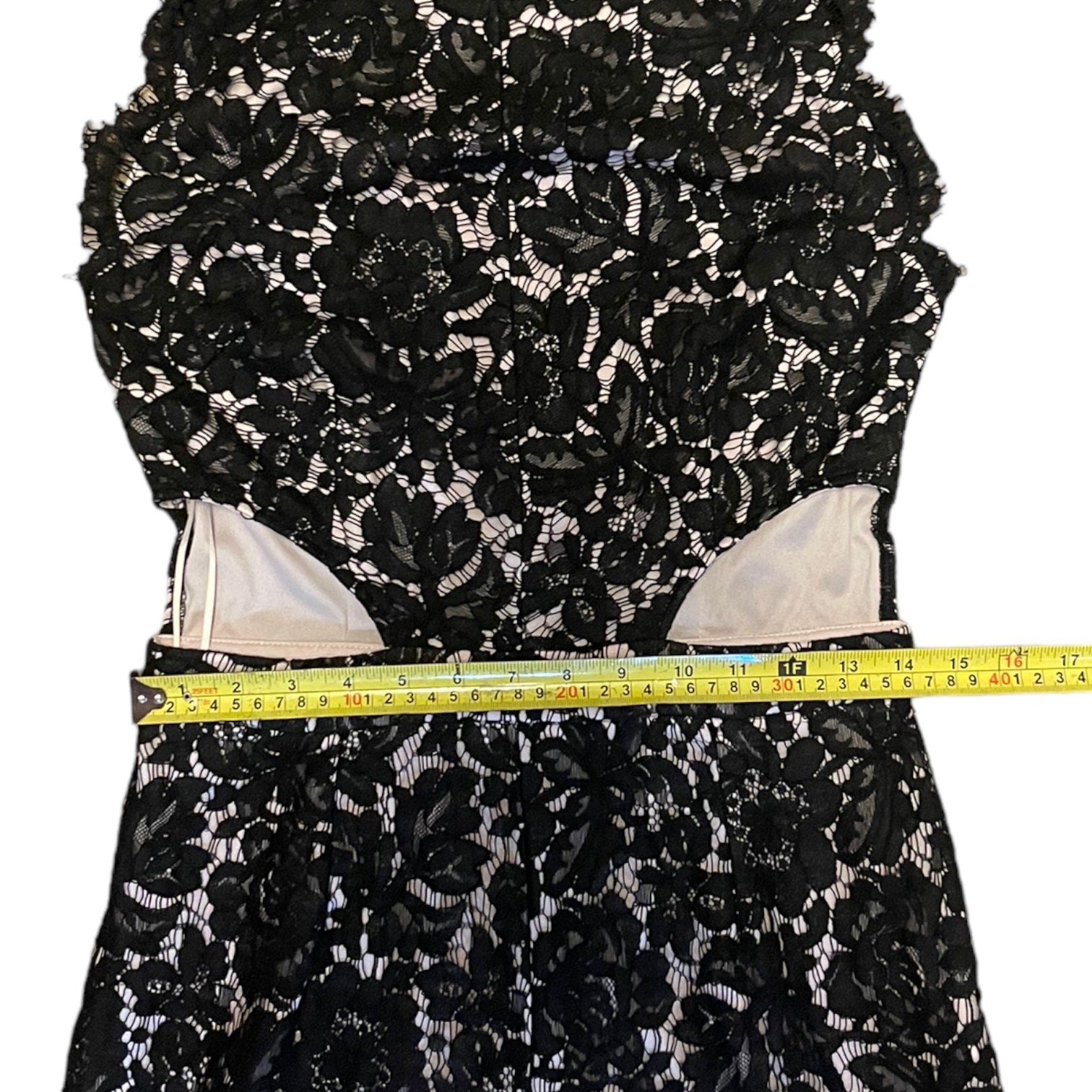 Black floral lace fabric with a measuring tape for scale on a white background