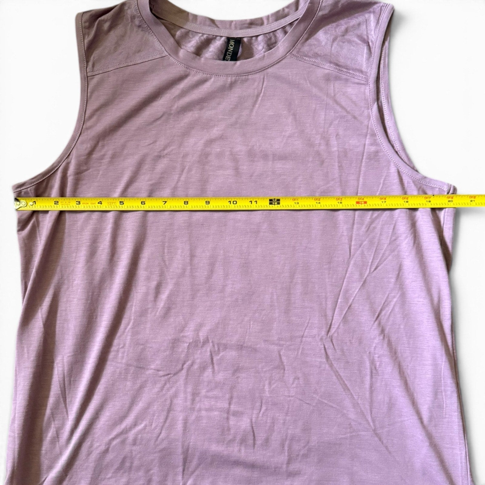 Purple shirt laying flat with a measuring tape laying across the top on a white background. 