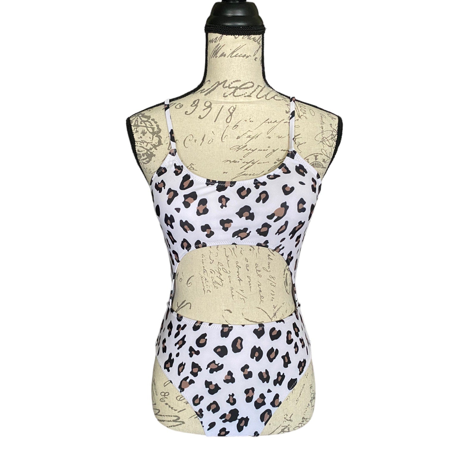 A sleeveless white monokini with a brown and black leopard print pattern, displayed on a beige script-printed dress form mannequin against a white background.