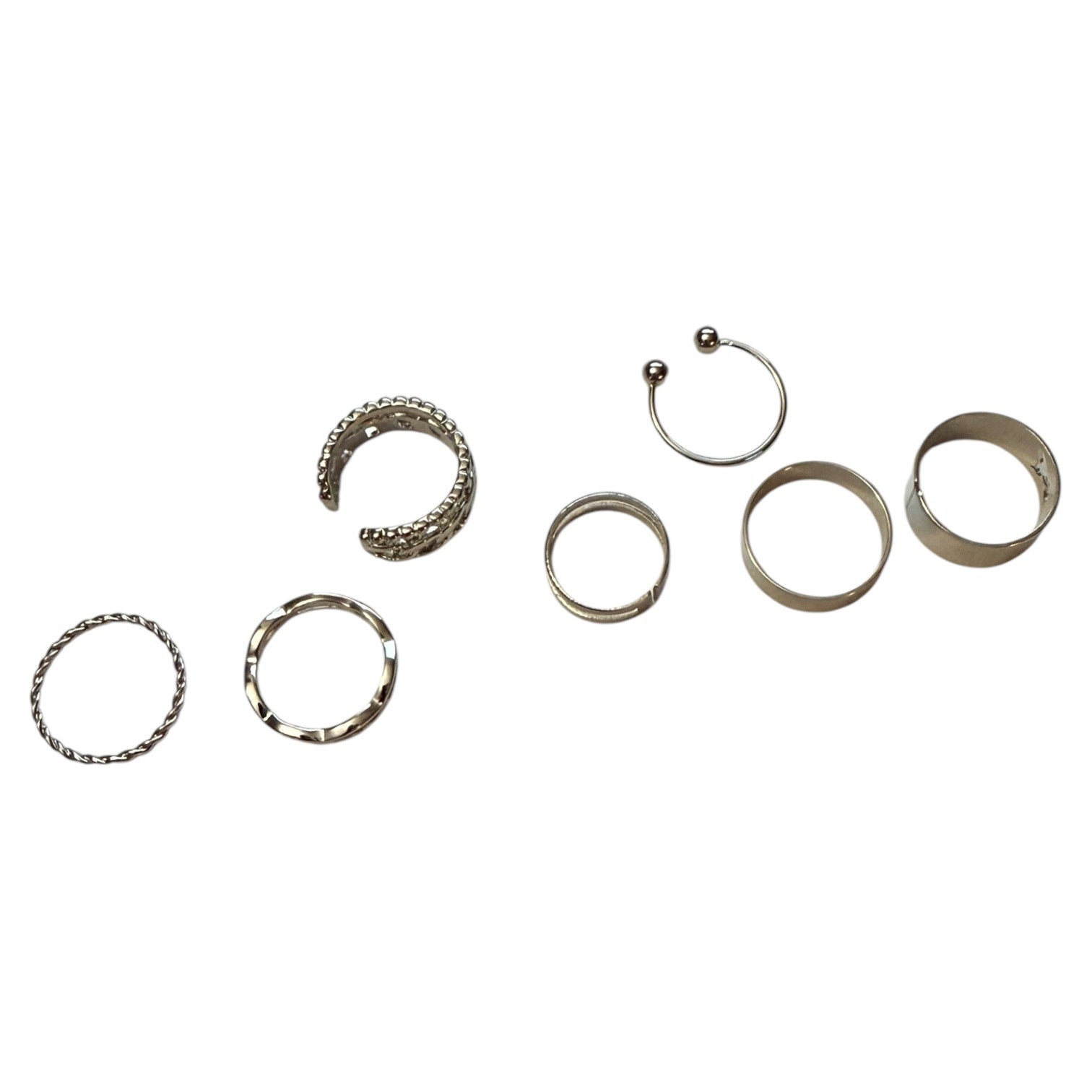 Seven silver-toned body jewelry rings, including two C-shaped cuffs, two flat rings, and two band rings, arranged on a plain white background.