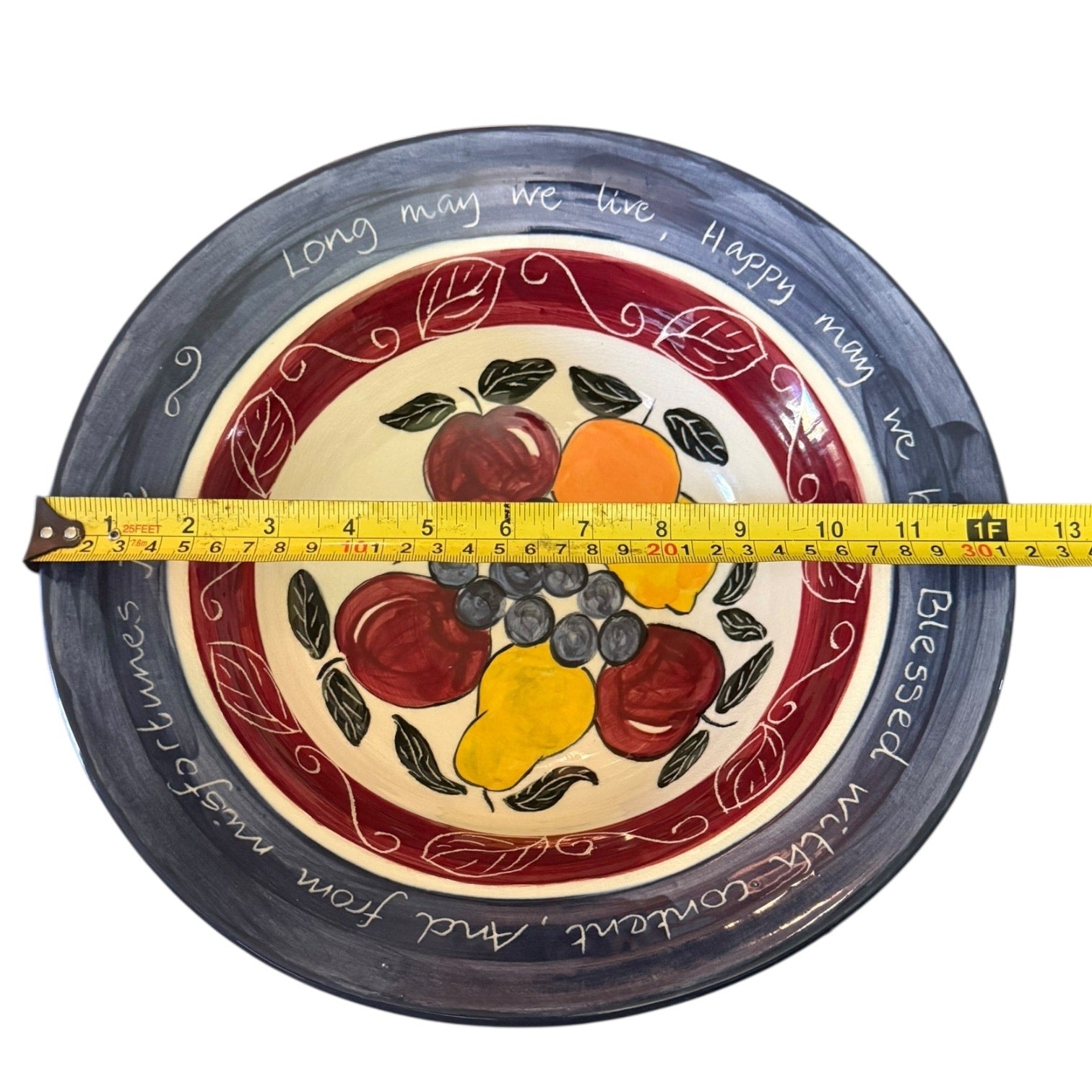 Decorative plate with fruit design and text, measured with a tape measure.