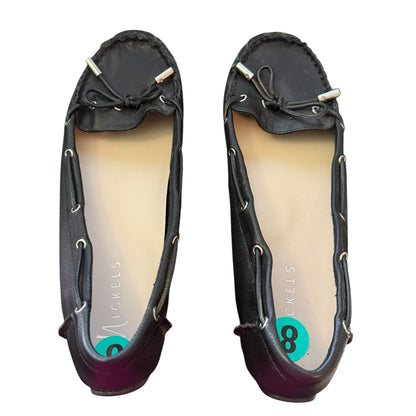 A pair of black leather moccasin-style flats with silver-tone eyelets and bow details, shown from a top-down view on a white background. 