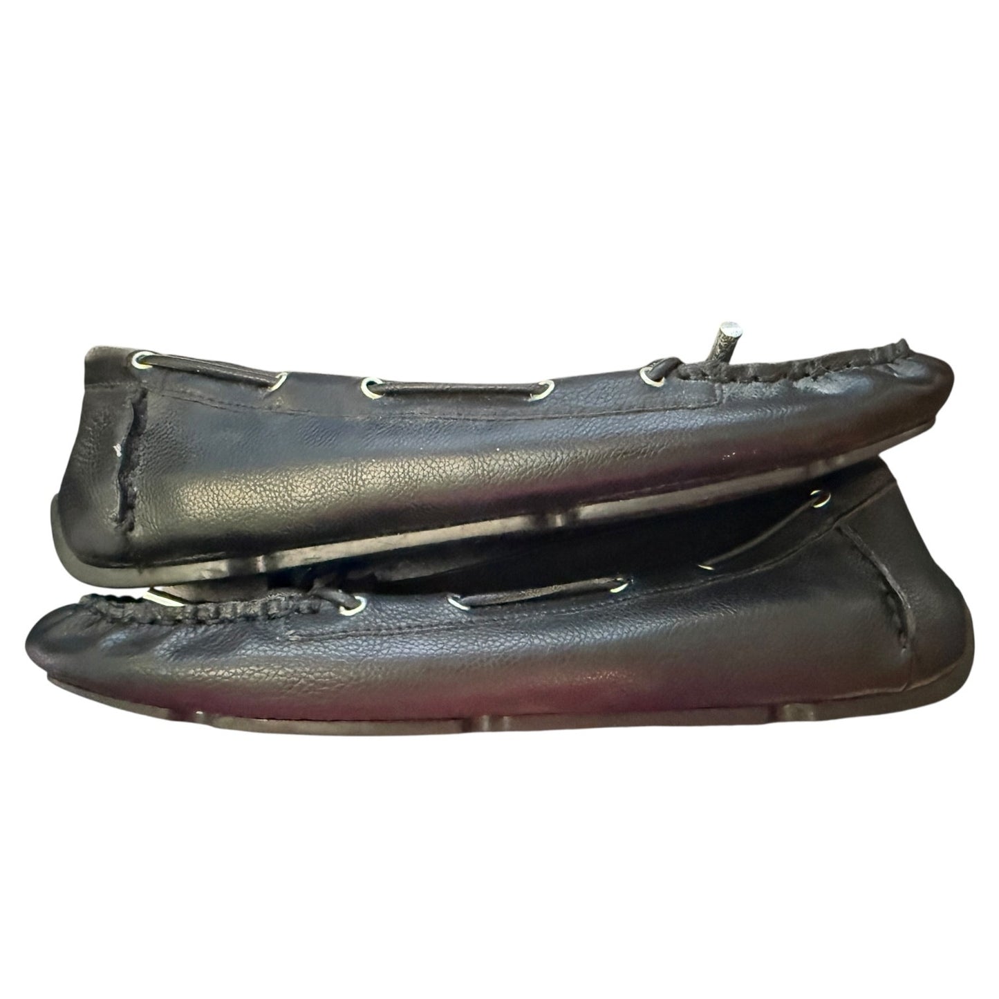 A pair of black leather moccasin-style flats with silver metal grommets shown against a plain white background.