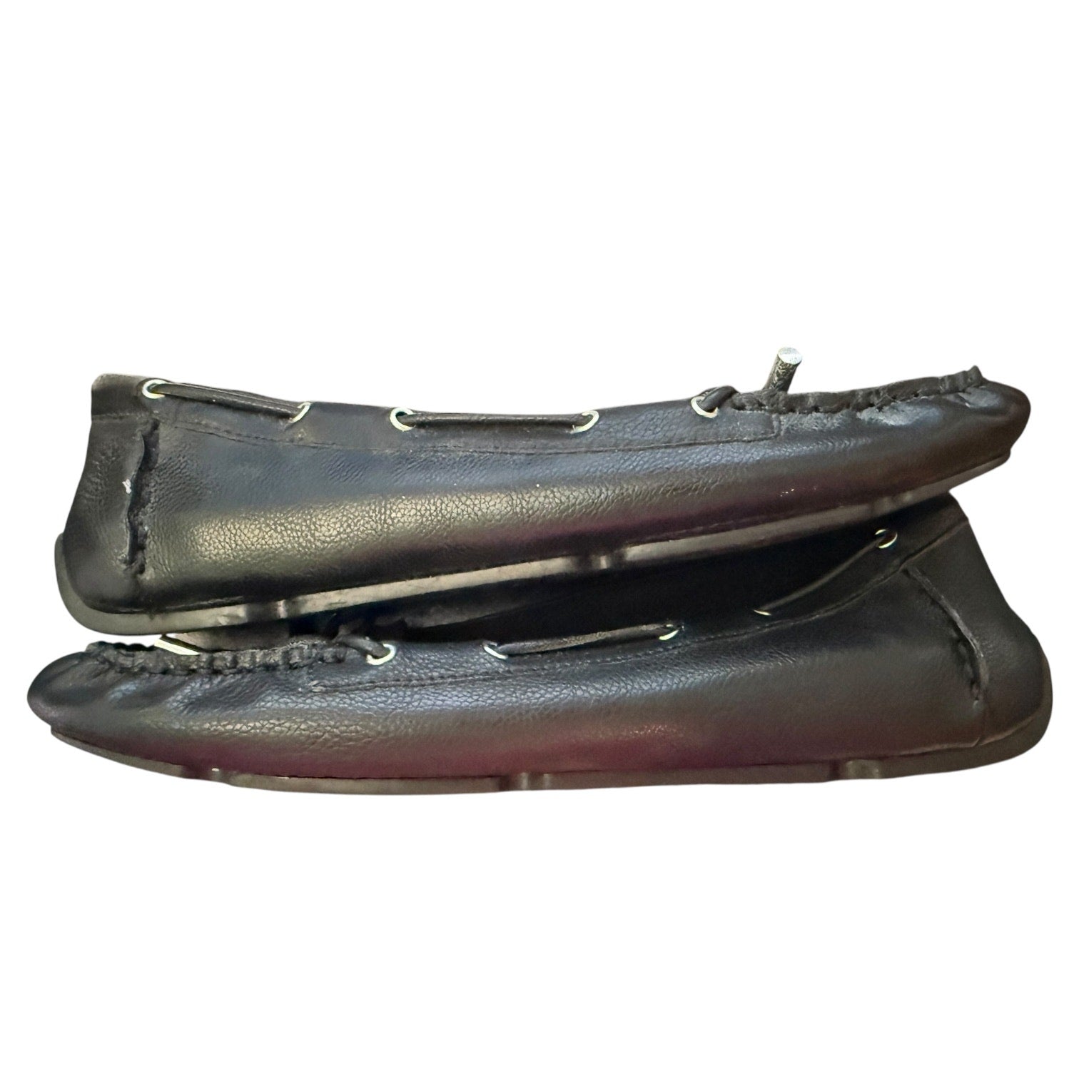 A pair of black leather moccasin-style flats with silver metal grommets shown against a plain white background.
