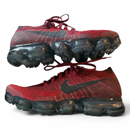 A pair of Nike Air VaporMax Flyknit sneakers in red and black, featuring a textured red Flyknit upper, black Swoosh, and translucent dark gray VaporMax air pods, shown against a plain white background.