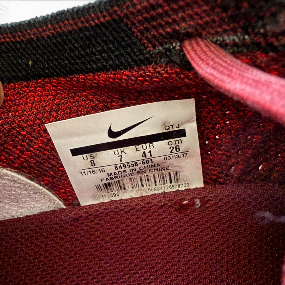 Close-up of a Nike shoe size 8 size tag on a red and black knit fabric shoe