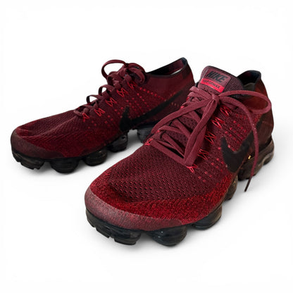 A pair of Nike Air VaporMax Flyknit sneakers in a deep burgundy red and black colorway, displayed on a clean white background.