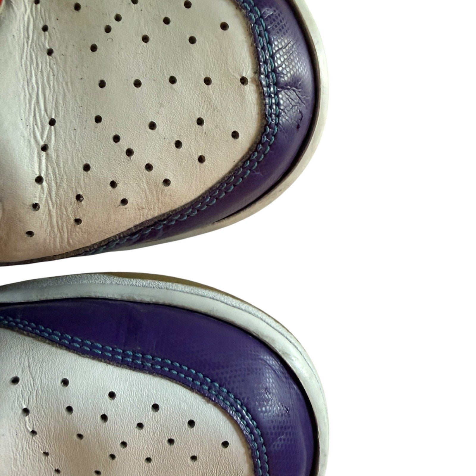 Close-up of a white shoe with purple sole and blue stitching on a white background