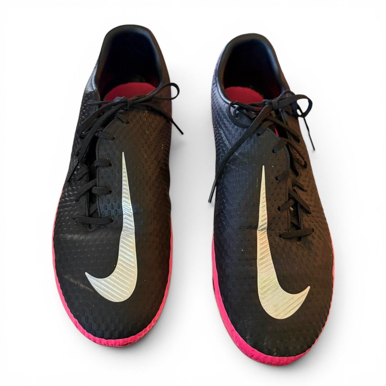 Black soccer shoes with pink soles and white Nike swoosh logo on a white background