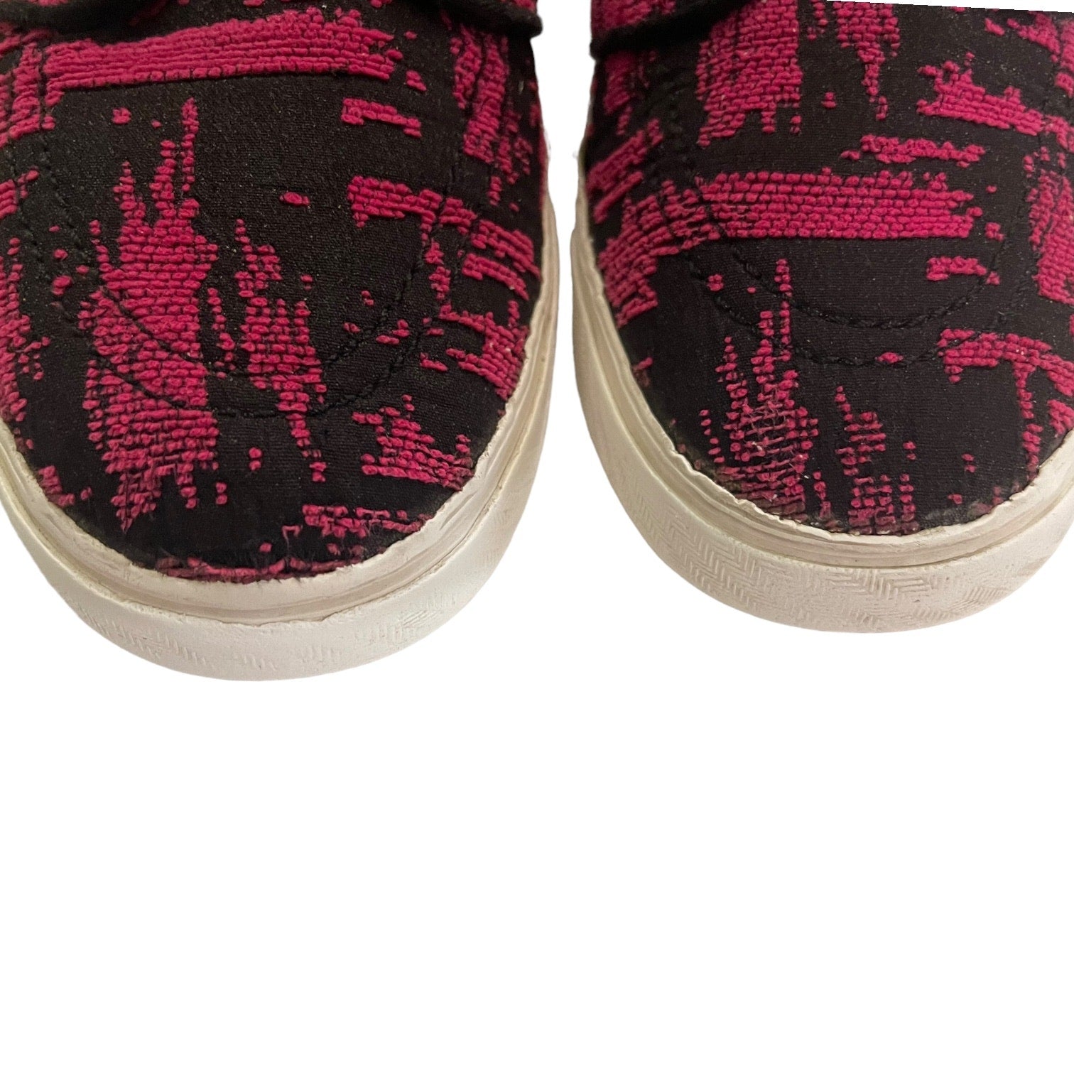 Close-up of the toe area of a pair of low-top sneakers, showing a black canvas upper with a vibrant pink abstract textured pattern and white rubber soles.