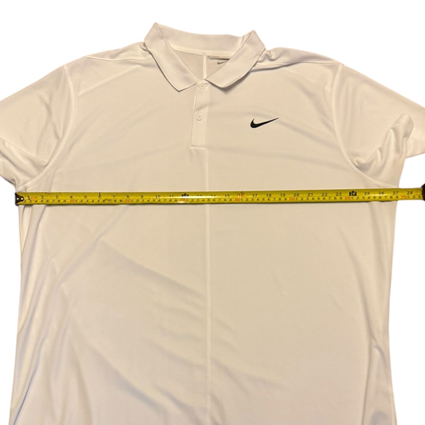 A white Nike polo shirt laid flat on a white background, with a yellow tape measure stretched horizontally across the chest to show the width.