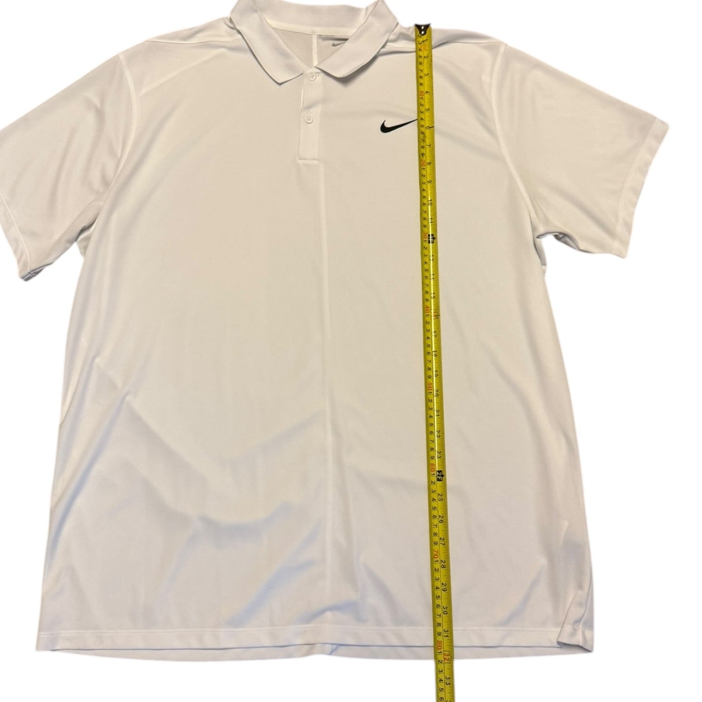 A white Nike short-sleeve polo shirt laid flat on a white background, with a yellow measuring tape vertically placed along the right side to show the garment's height.
