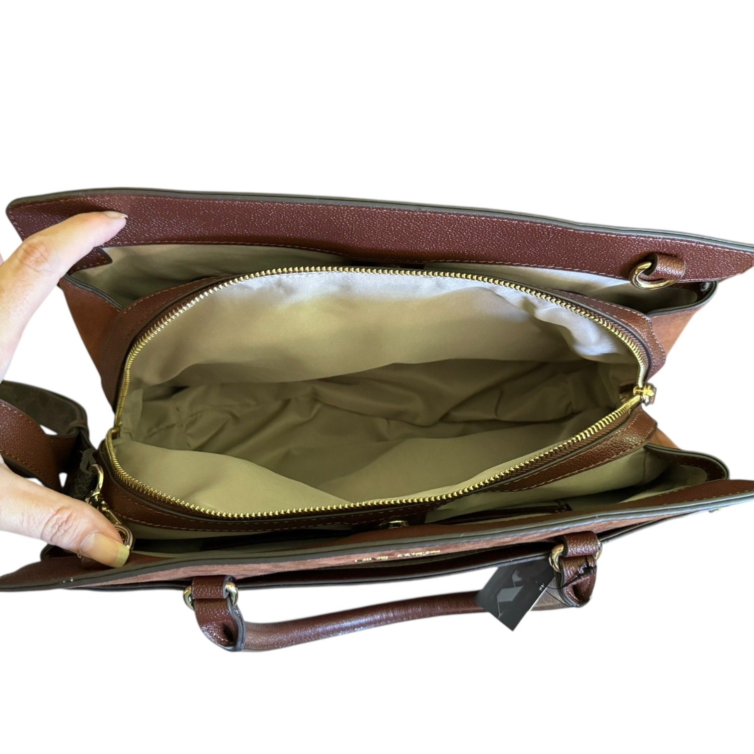 Brown leather handbag interior with gold zipper being held open on a white background