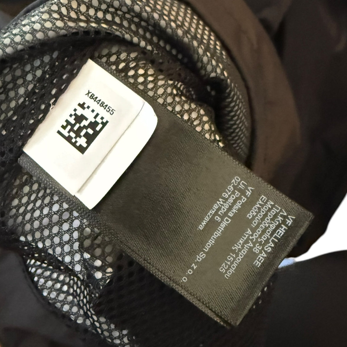 Close-up of a garment's interior label area showing a dark fabric brand tag and a white size/QR code label attached to black mesh lining.