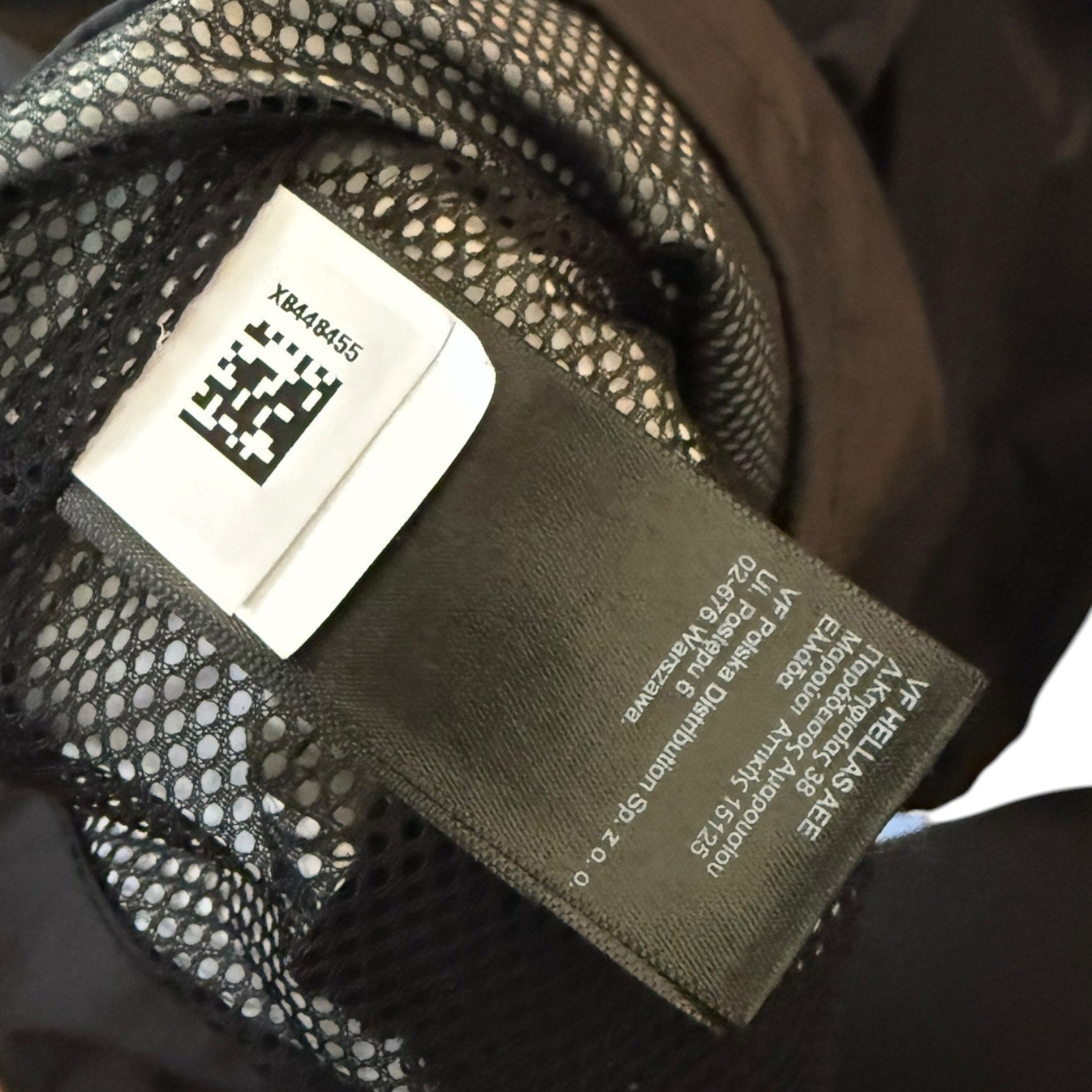 Close-up of a garment's interior label area showing a dark fabric brand tag and a white size/QR code label attached to black mesh lining.