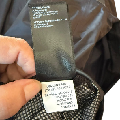 Close-up of a garment's interior label area showing a black size/manufacturer label and a white style information tag attached to dark mesh fabric.
