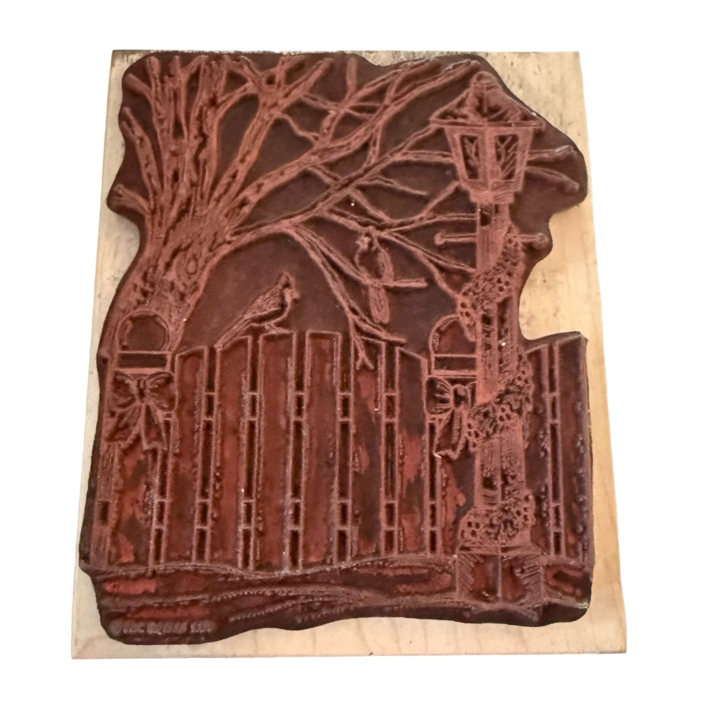 A rubber stamp featuring a tree with bare branches, a fence, birds, and a lamppost, shown on a light wood backing against a white background.