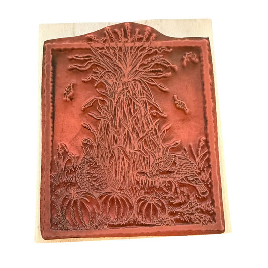A square wooden stamp block with a carved autumn scene featuring pumpkins, a cornstalk, birds, and a turkey, shown on a white background.