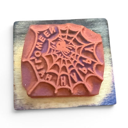 Wooden stamp with spider web design and 'Happy Halloween' text on a wooden block.