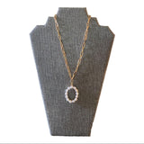 Gold chain necklace with a circular pearl pendant on a gray bust