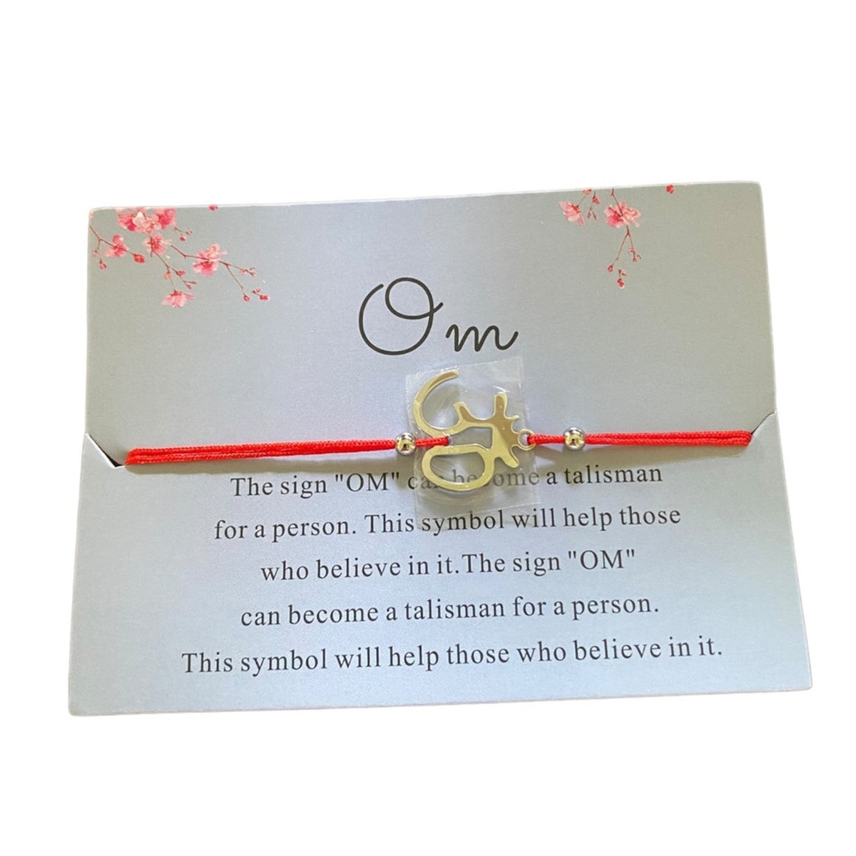 A red string bracelet with a silver Om symbol charm, presented on a silver card with printed text and floral details.