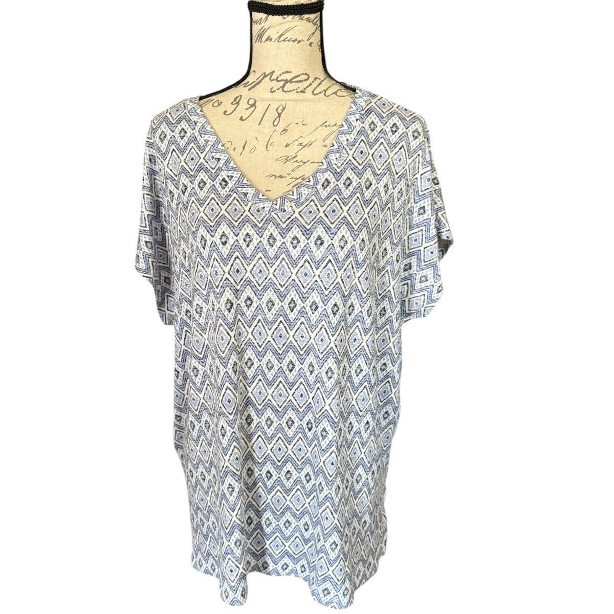 A short-sleeve V-neck top with a blue, white geometric diamond pattern, displayed on a vintage-style beige dress form mannequin against a white background.