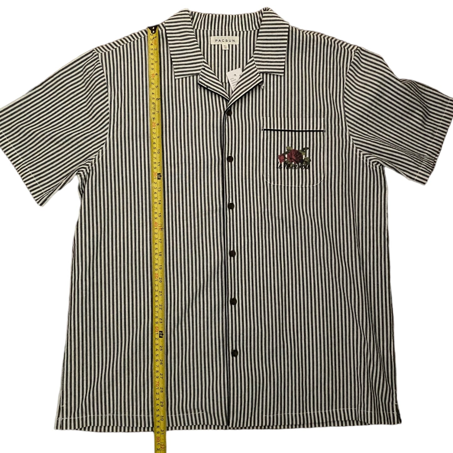 Gray and white striped shirt with a pocket and logo, measured by a tape measure on a white background.