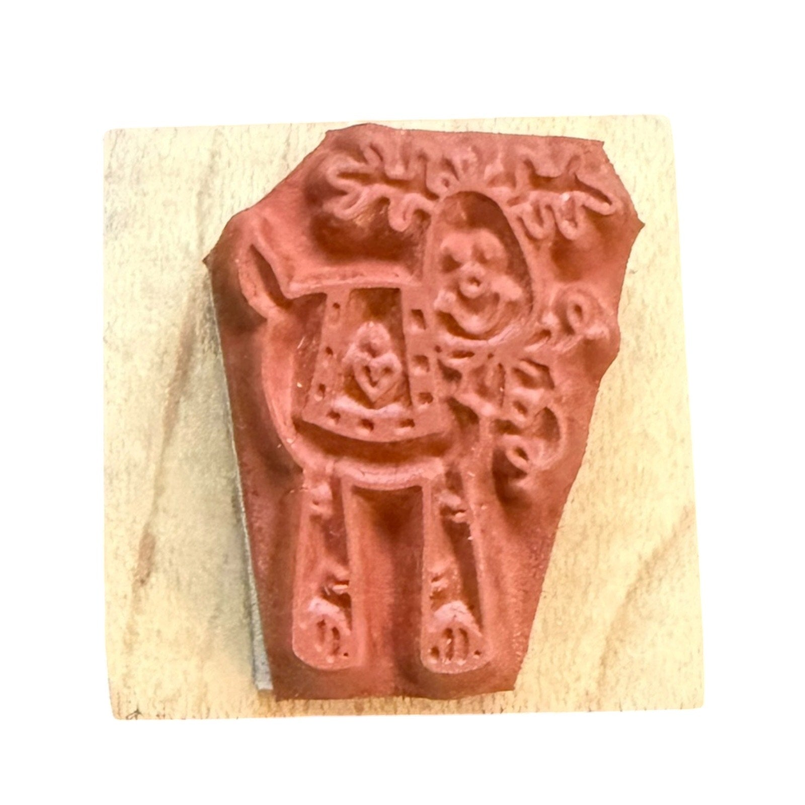 A terracotta-colored rubber stamp , mounted on a light-colored wooden block against a white background.
