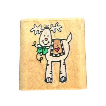 A square wooden craft block featuring a cartoon reindeer with white antlers, a green holly leaf, and a brown patterned blanket with a red heart, set against a plain white background.