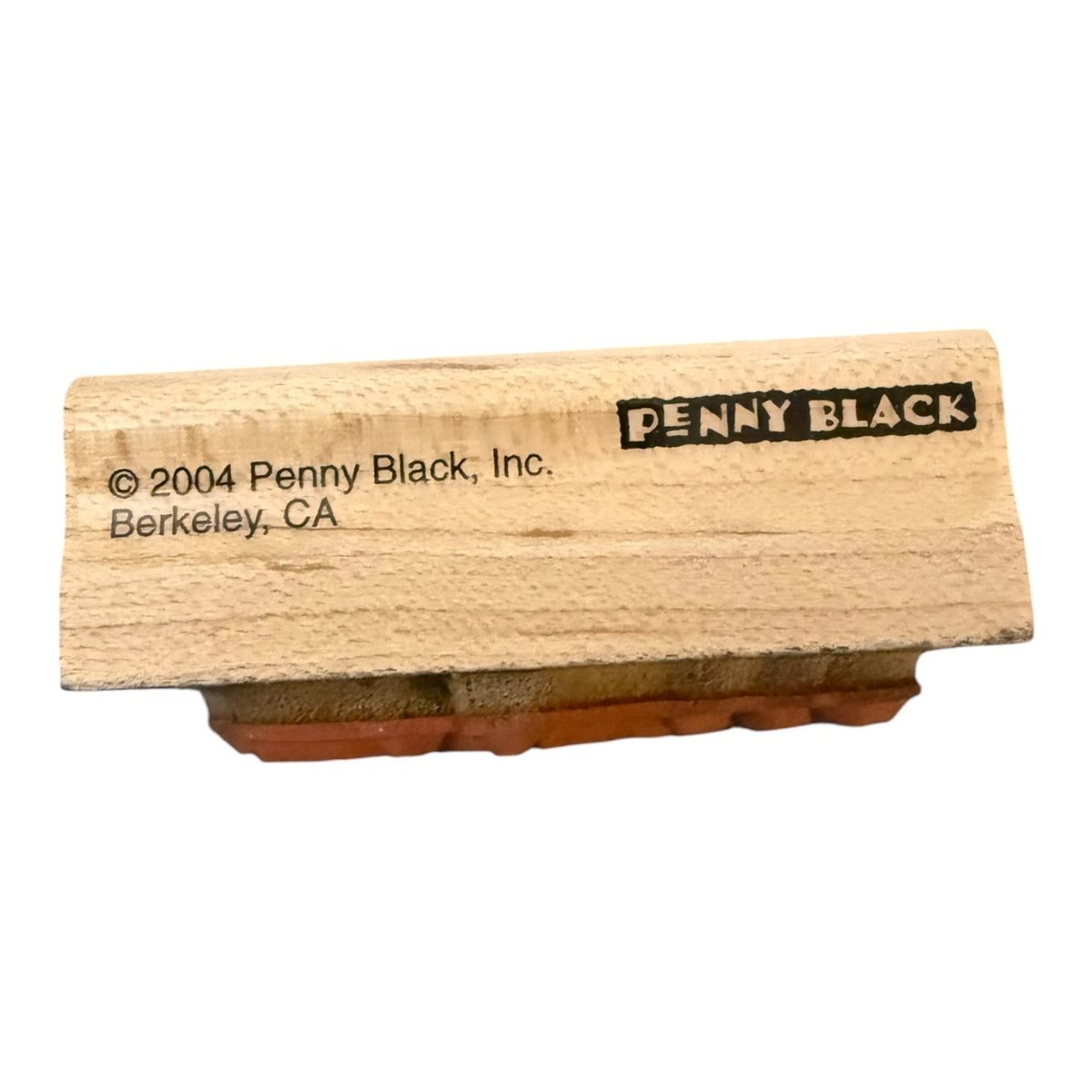 A wooden rubber stamp block with a black inked face, showing the brand name 'PENNY BLACK' and copyright text on the wood, photographed against a plain white background.
