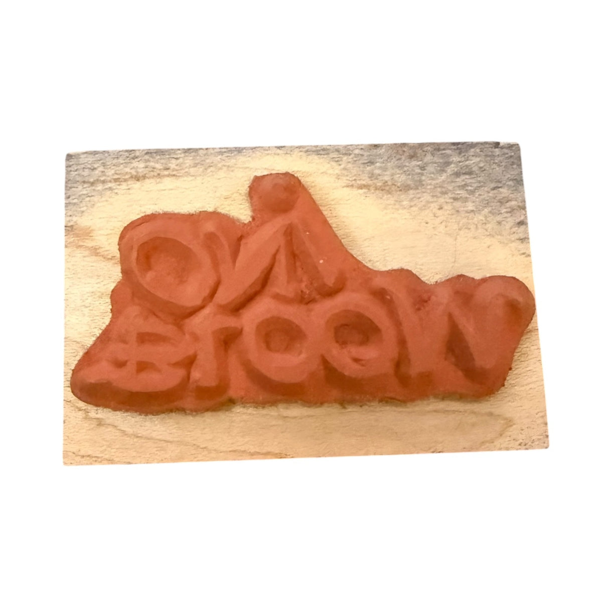 A terracotta-colored rubber stamp , mounted on a light-colored wooden block against a plain white background.