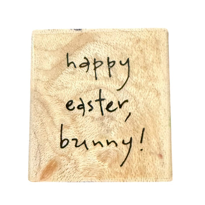 A square wooden plaque with a natural light tan wood grain texture, featuring the handwritten black text 'happy easter, bunny!' on a plain white background.