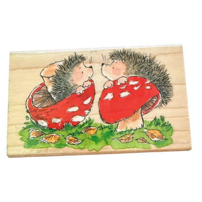 2 hedgehogs sitting with mushrooms on a wood block stamp on a white background. 