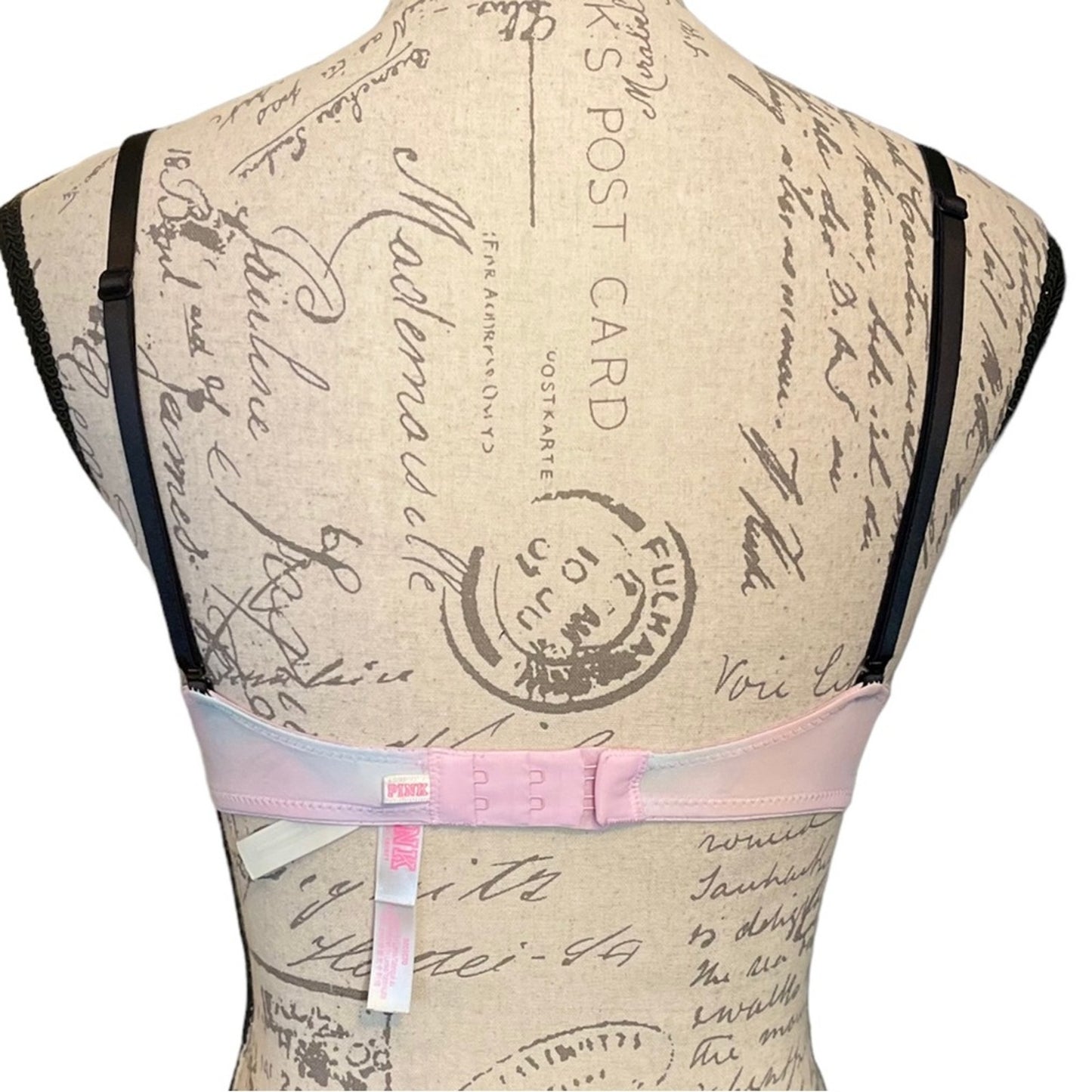 Bra with pink & blue band on a mannequin against a vintage postcard background