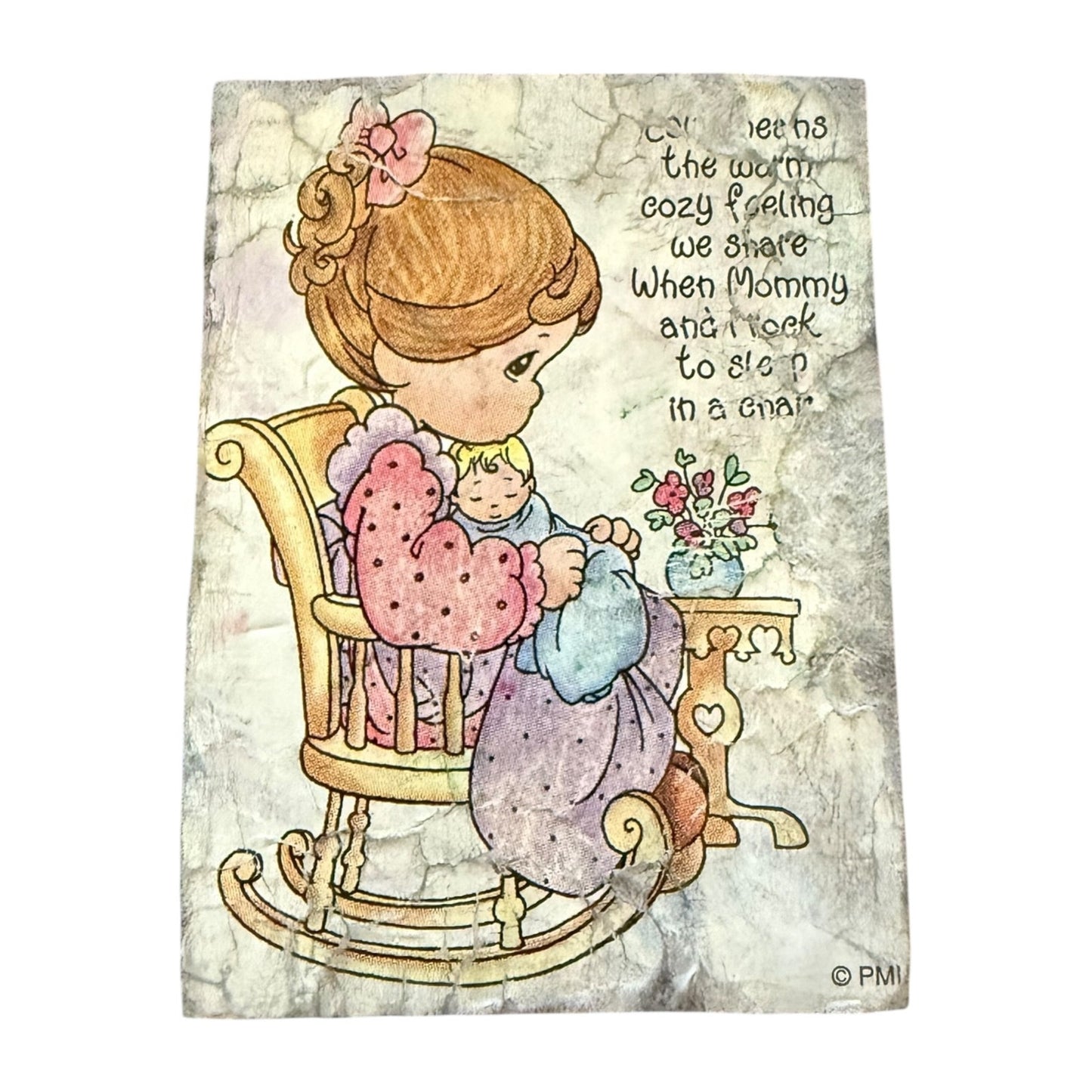 A foam rubber stamp of a young girl in a rocking chair holding a teddy bear, with handwritten text on the right side and a small flower arrangement. on a white background