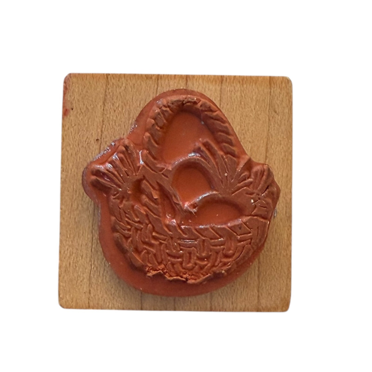 A rubber stamp with a detailed design, mounted on a square light brown wooden block, set against a plain white background.