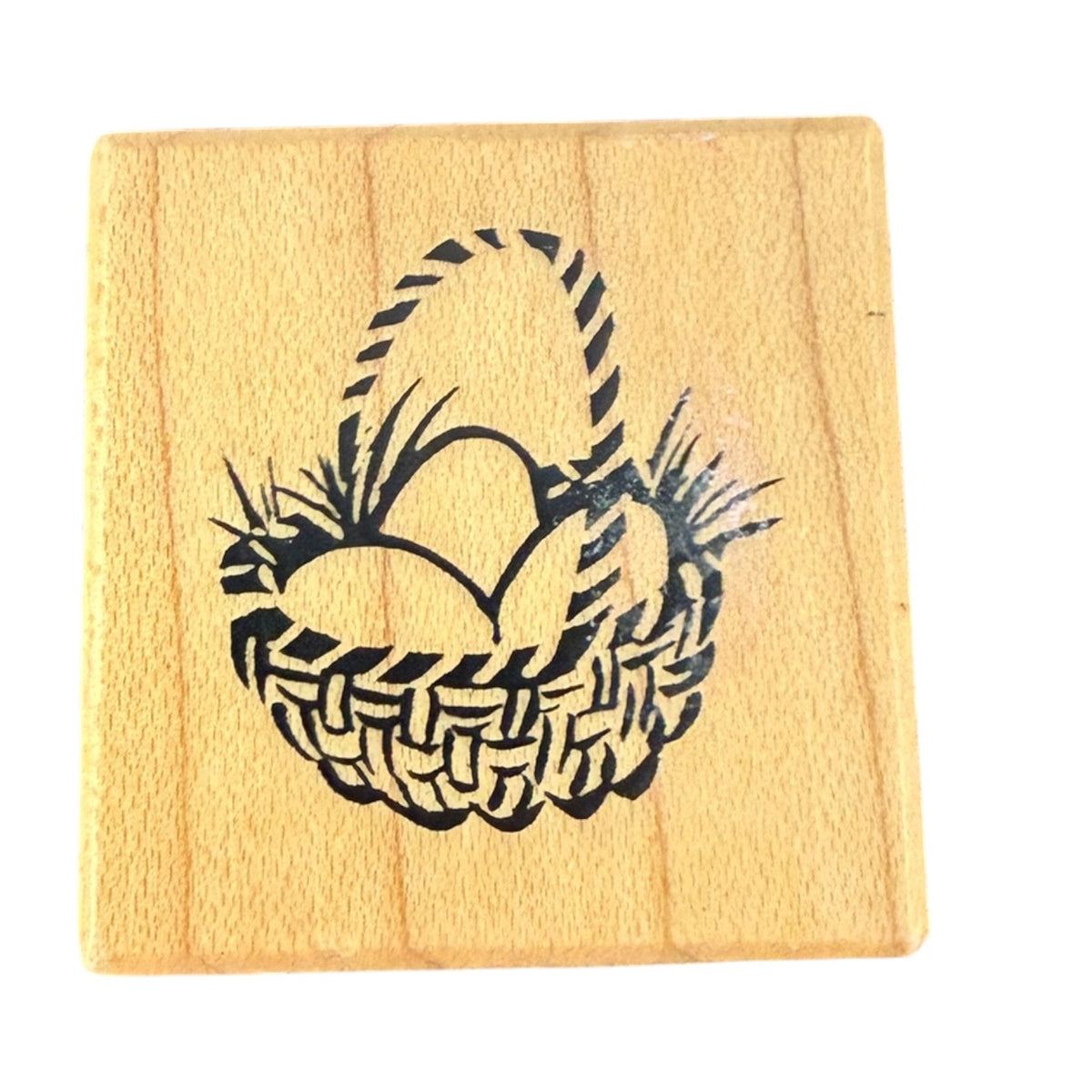 A square wooden rubber stamp featuring a black design of a woven basket holding Easter eggs, shown on a plain white background.