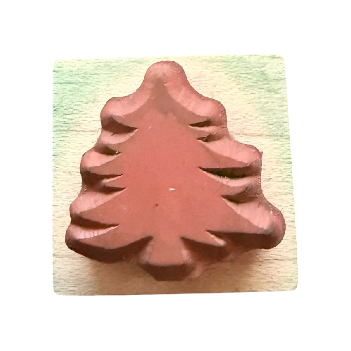 A Christmas tree-shaped stamp  on a light wood block shown against a plain white background.