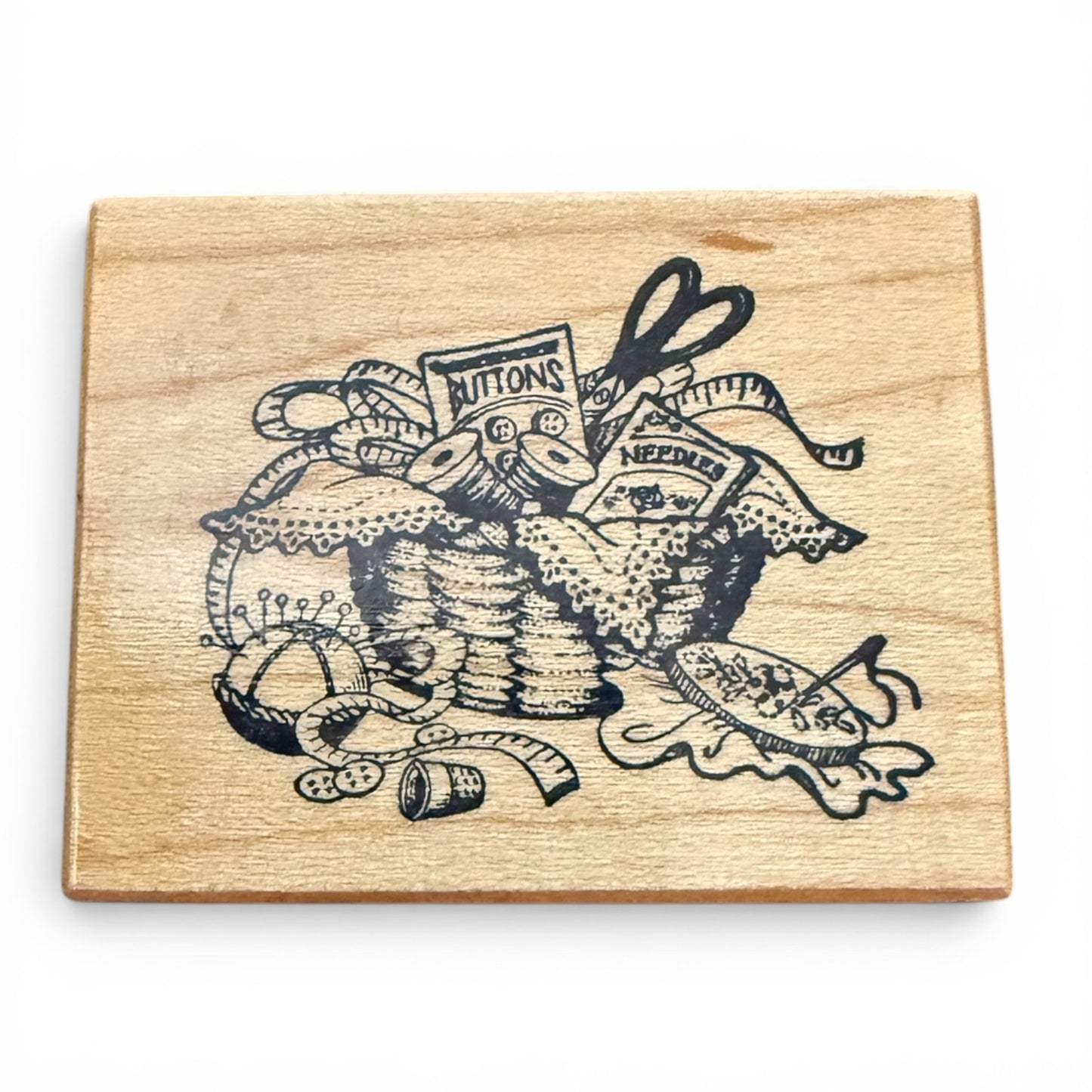 Wooden block with black ink design of sewing supplies on a white background