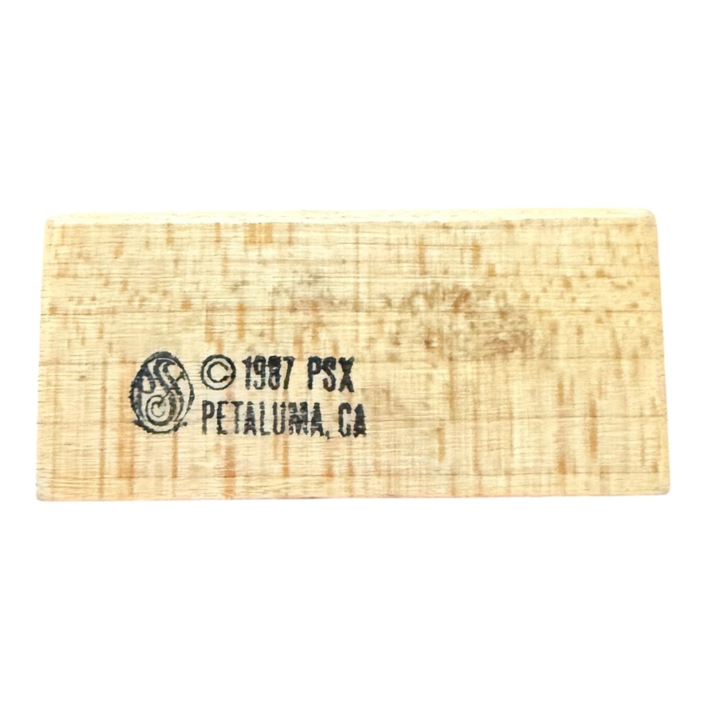 A wood block stamp with a black printed logo and text reading '© 1987 PSX PETALUMA.CA' on a plain white background.